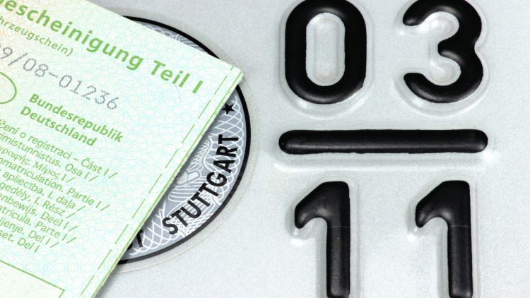 Auf dem Teil eines Saisonkennzeichens liegt angeschnitten ein Fahrzeugschein