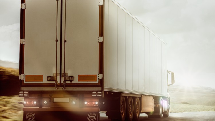 Im Bild fährt ein Lkw. Strahlende Sonne von vorne sorgt für Lichtreflexe, die ihn etwas unwirklich erscheinen lassen, so als könnte er gleich im Licht verschwinden