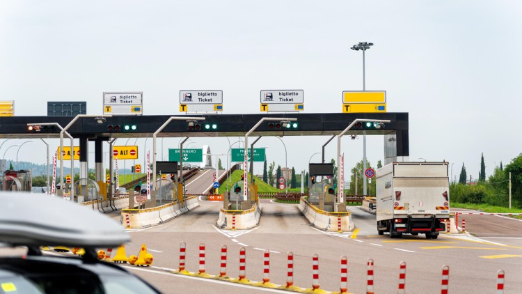 Die Mautstation Affi in Italien passieren Fahrzeuge auf dem Weg Richtung Brenner. Schranken, Ticketautomaten und Fahrspuren zeigen den Verkehrsfluss auf der italienischen Autobahn. Auf dem Bild nähert sich ein weißer Lkw der Mautstation auf der äußeren Fa