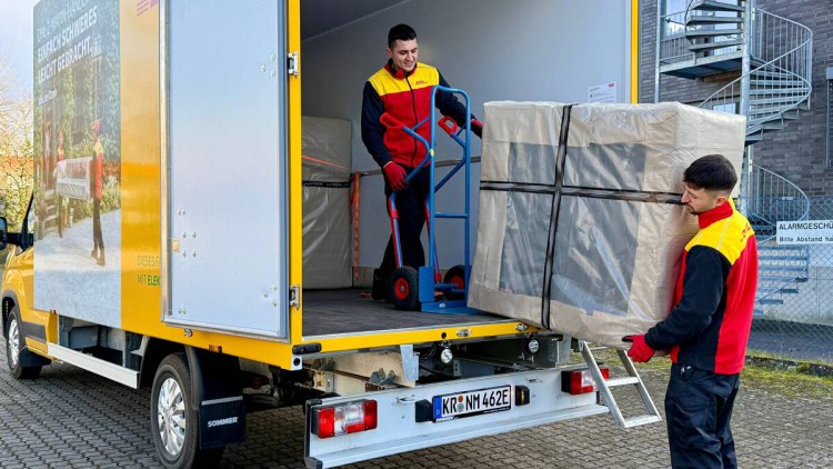 Zwei Mitarbeiter von DHL 2-Mann-Handling laden ein verpacktes Möbelstück aus ihrem Transporter