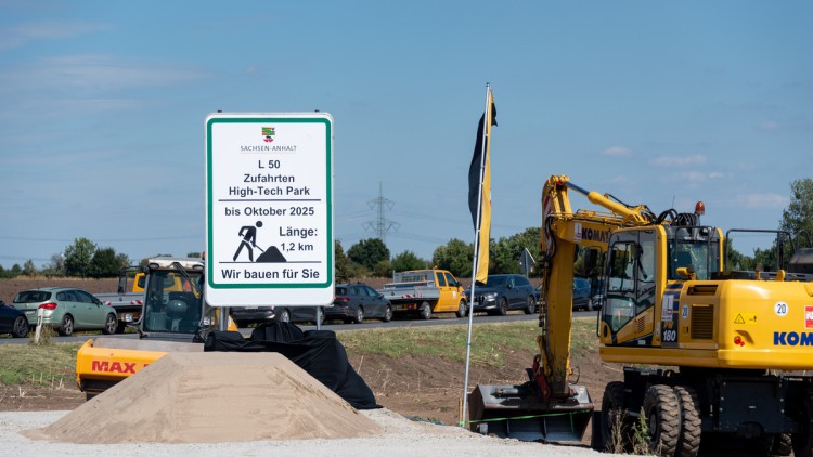 Baumaschinen stehen an der Zufahrt zu einem Acker. Links daneben weist ein Schild auf den Ausbau der Landesstraße 50 hin. Von dieser Landesstraße werden Zufahrten zum High-Tech-Park auf dem Eulenberg abzweigen. Dort wollte der US-Chiphersteller zwei Halbl