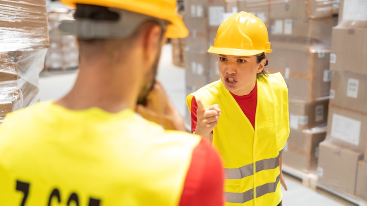 Im Bild eine wütende Lagermitarbeiterin, die mit dem Zeigefinger auf einen Kollegen zeigt. Der Streit könnte noch eskalieren, aber auf dem Bild ist es bisher nur bei Worten geblieben