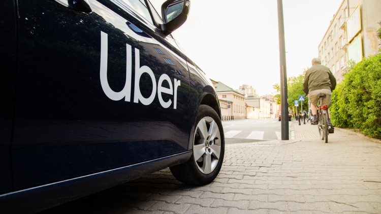 Blick auf ein parkendes oder haltendes Auto mit Uber-Logo auf einer Straße in Warschau, Polen. Auf dem Bürgersteig fährt ein Radfahrer und weiter weg sind Fußgänger zu sehen
