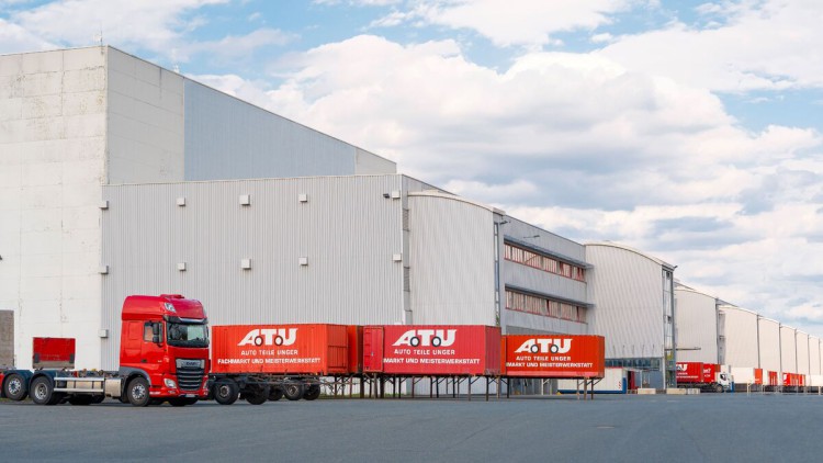 Vor einer großen Lagerhalle stehen viele Lkw und Container von ATU in rot