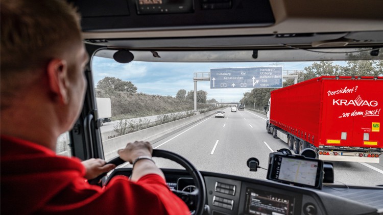 Lkw-Fahrer am Steuer sieht auf der Autobahn Lkw mit KRAVAG-Logo vor sich