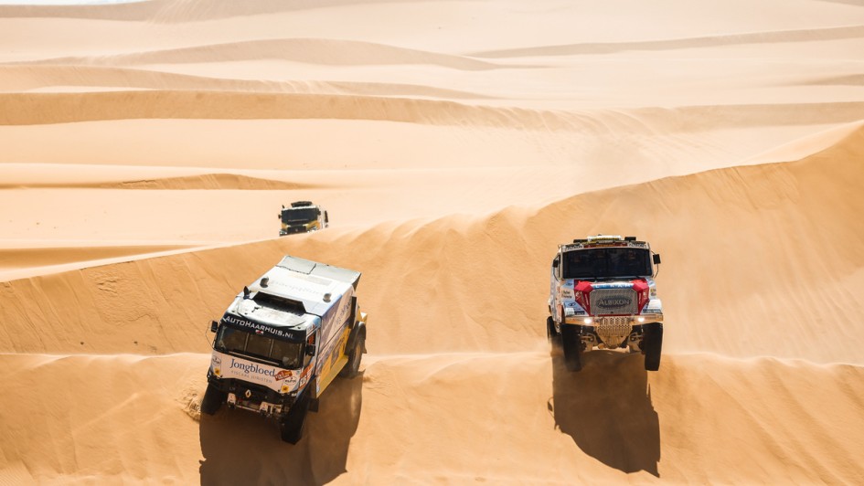 Drei Rallye-Lkw befahren nebeneinander eine Sanddüne 