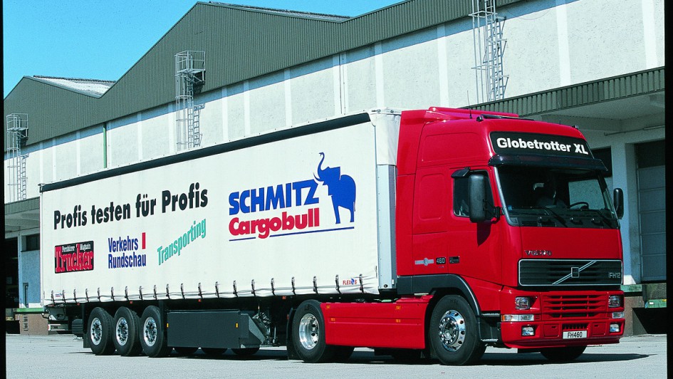 Ein rot lackierter Volvo FH 460 parkt vor einer Lagerhalle. Die Sattelzugmaschine zieht einen weißen Auflieger